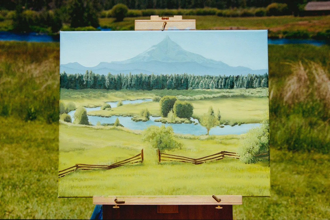 Finished landscape painting of Mt. Hood, river, and meadow on an easel