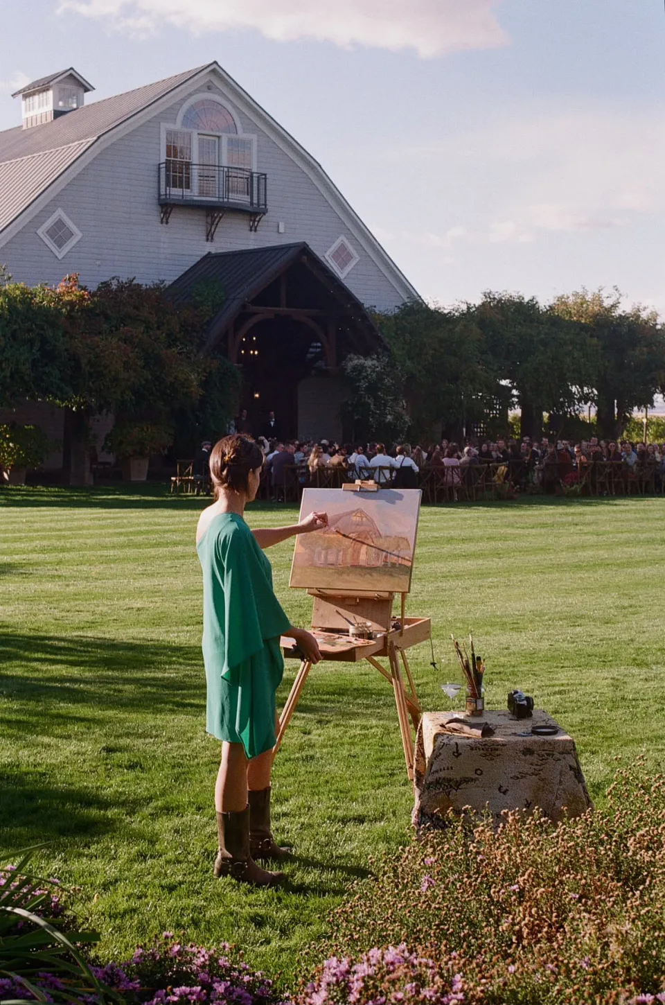 Holly Di Cecco painting the barn venue live on an easel while wedding guests are seated behind her